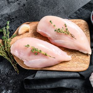 Raw chicken breast fillet on a chopping Board with herbs and spices. Black background. Top view.